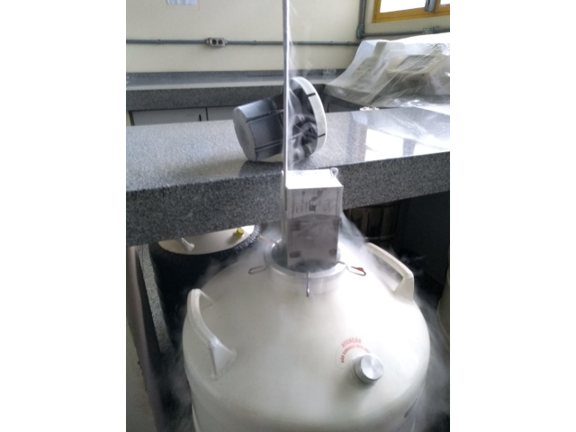 Foto do tambor de criopreservação com o suporte de metal em que ficam as amostras sendo levantado da imersão em nitrogênio líquido, ocasionando a formação de uma leve névoa devido à evaporação do nitrogênio.