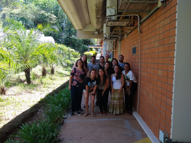 12 pessoas da equipe do laboratório, em pé, ao lado do Departamento de Botânica da UFSCar. Foto tirada em 2019.